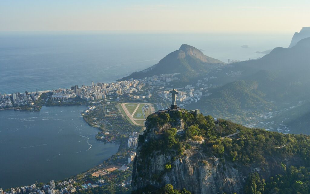 Vista aérea da lateral do Cristo Redentor no topo do Morro Corcovado, ao fundo o morro dos cabrietos e a lagoa Rodrigo de Freitas